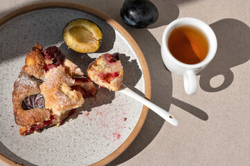 Piece of The Famous Plum Torte, pie bitten on plate with teaspoon and cup of tea. Traditional american fruit cake bakery