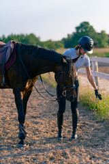 A helmeted rider leads her beautiful black horse by the harness in the riding arena during a horseback ride