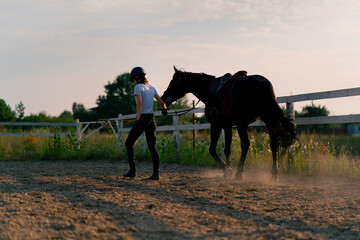 A helmeted rider leads her beautiful black horse by the harness in the riding arena during a...