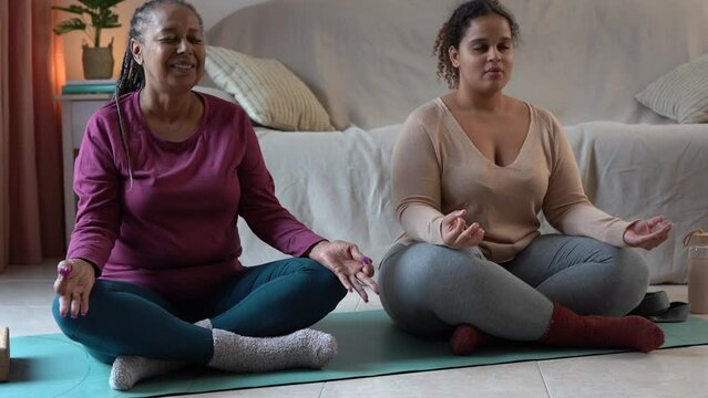 African mother and adult daughter doing yoga meditation exercise together at home
