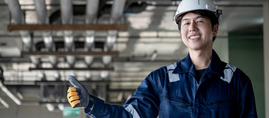 Portrait of Asian confident man construction worker in protective uniform suit and safety helmet showing thumbs up in unfinished building. Male engineer showing hand gesture sign at construction site