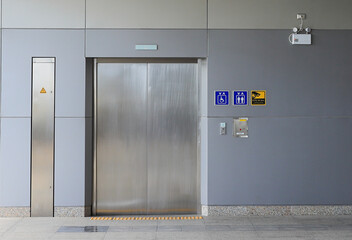 Hallway with LCD screen floor stand, Modern steel elevator cabins, closed elevator doors.