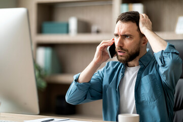 Portrait of stressed young businessman talking on cellphone in office