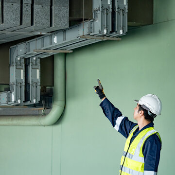 Building inspector man checking telephone cable duct wireway. Asian male maintenance worker with reflective vest and safety helmet pointing at wire way working for communication system inspection