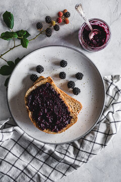 vista superior de unas tostadas con mermelada de mora en un plato, con algunas moras, un frasco con mermelada y una rama de zarzamora