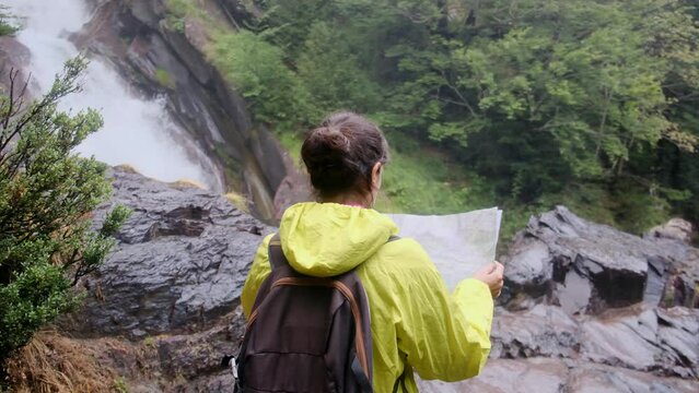 40 year old woman alone in the forest mountain with waterfall using map to orient herself and find way. Concept of freedom, empowerment, personal development, finding one's own path and adventure 