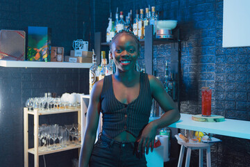 Black waitress poses and looks at the camera on the bar of a pub