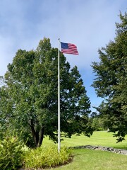 American flag waving in the wind with trees and blue sky in the background