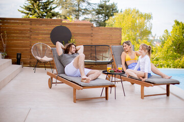 Family with a mother, father and daughter sitting on the deck chairs by the swimming pool