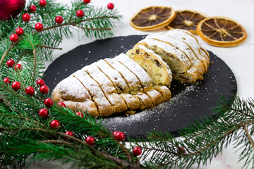 The stolen is cut into slices. Classic German cupcake on a black plate. Plate surrounded by Christmas tree branches