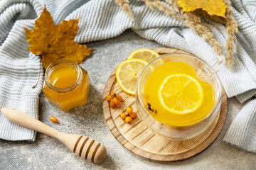 Hot herbal vitamin sea buckthorn tea in a glass cup with fresh sea buckthorn berries, honey and lemon on a stone tabletop. Relaxation and herbal medicine.