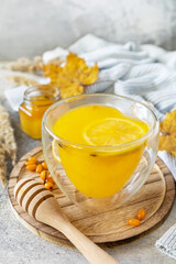 Hot herbal vitamin sea buckthorn tea in a glass cup with fresh sea buckthorn berries, honey and lemon on a stone tabletop. Relaxation and herbal medicine.