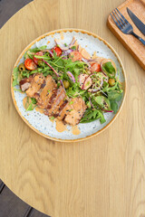 A plate with veal meat on greens with vegetables and olives under nut sauce on a wooden table top view