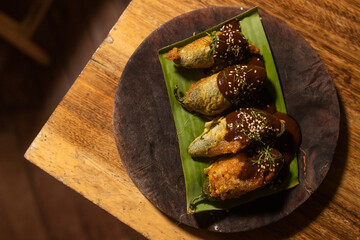 Top down view of traditional Mexican dish with breaded green Chile and mole salsa with sesame seeds served on top of banana leaf in wooden plate 