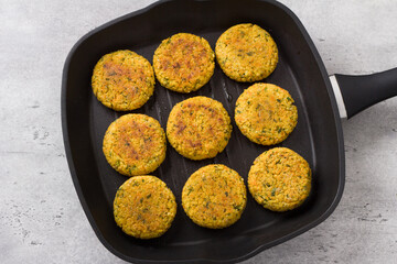 Vegan millet cutlets with carrots, greens and seeds in a frying pan on a gray textured background, top view. Homemade vegan food