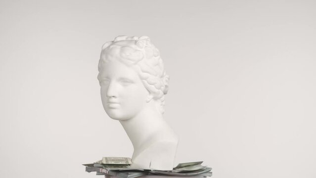 Closeup shot. Ancient marble bust statue of roman era woman with money bills spinning round on a platform. Isolated on blue background. HDR BT2020 HLG Material.