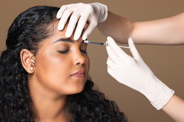 Cosmetologist making botox injection in interbrow zone to latin chubby woman getting anti-wrinke...
