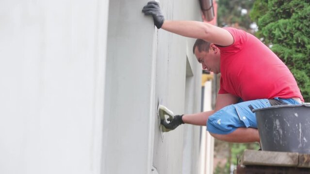 Young man worker application of glue or adhesive on the facade of the house, insulation of the house