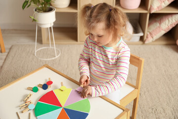 Cute little girl playing matching game with clothespins at home