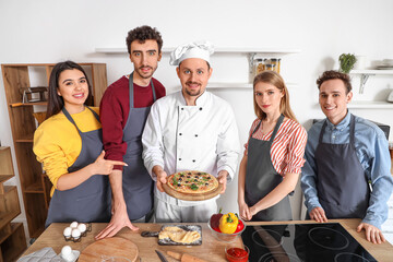 Italian chef with prepared pizza and group of young people after cooking class in kitchen
