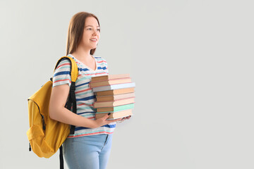 Female student with stack of books on light background