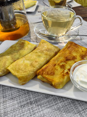 Fried pancakes stuffed with meat and sour cream. Placed on a rectangular white plate. View on the background of tea. Close-up.
