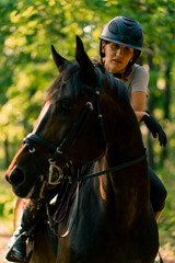 Obraz premium A rider dressed in a helmet rides her beautiful black horse in the forest during a horseback ride