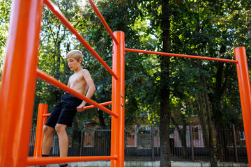 A child athlete sits on the bars of a sports field. Street workout on a horizontal bar in the school park.
