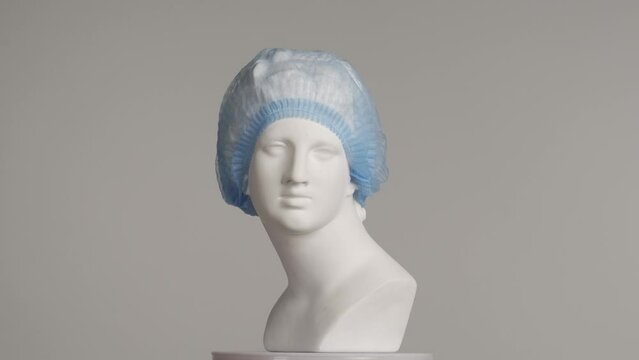 Closeup shot. Ancient marble bust statue of roman era woman in medical bouffant spins on a platform. Isolated on grey background. HDR BT2020 HLG Material.