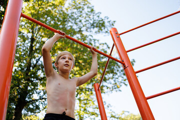 Bottom view of a gymnast boy holding on to a sports bar. Street workout on a horizontal bar in the school park.