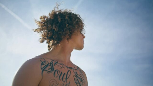 Handsome man surfer posing at sunny sky backdrop close up. Guy holding surfboard
