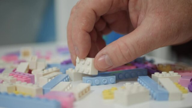 Blurred Shooting with an Elderly Person Playing Like a Child with Colorful Small Toy Bricks on the Table.