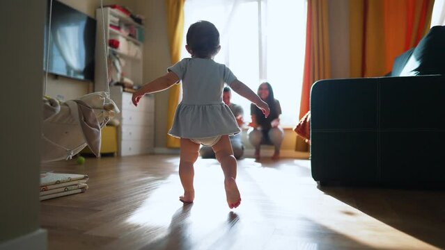 Baby first steps.Child kid runs across floor to family.kid learn to walk and run with help of his parents.Happy family at home first steps of toddler.father encourages baby teaches to take first steps