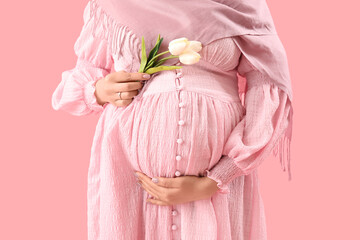 Young pregnant Muslim woman with tulips on pink background, closeup