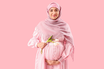 Young pregnant Muslim woman with tulips on pink background