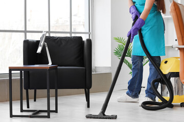 Female janitor vacuuming floor in office - obrazy, fototapety, plakaty