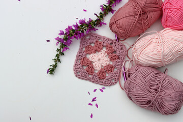 Pink crocheted granny square, soft  cotton yarn balls of different pink color shades. White background with copy space. Spring crochet concept. 