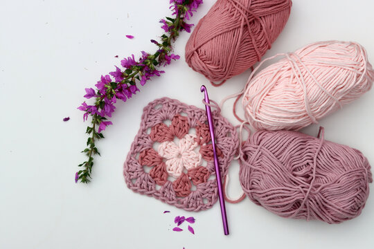 Pink crocheted granny square, soft  cotton yarn balls of different pink color shades. White background with copy space. Spring crochet concept. 