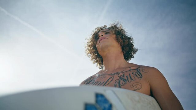 Attractive happy surfboarder standing in front beautiful blue sunny sky close up