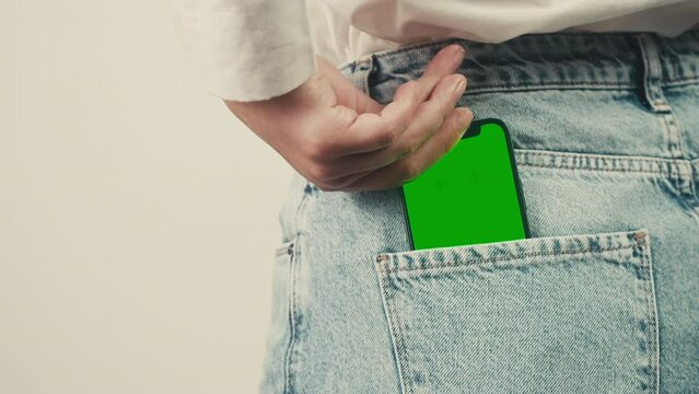 Smartphone phone with a green screen chroma key in the back pocket of jeans pants. Phone with chroma key close-up.