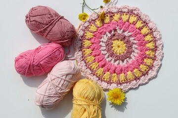 Crocheted pink and yellow mandala on white background with copy space. Top view photo of cotton...