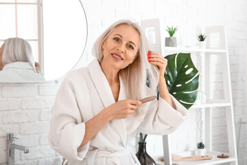 Mature blonde woman brushing hair in bathroom