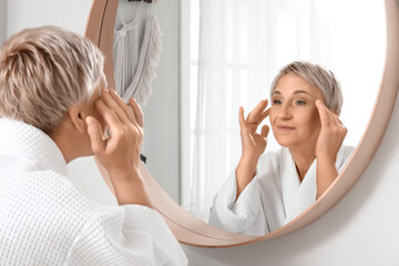 Mature woman massaging her face near mirror in bathroom