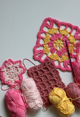 Different crocheted elements on white background with copy space. Handmade home decoration. Beautiful pink and yellow cotton yarn balls. Arts and crafts concept. 