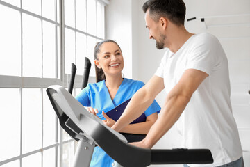 Female physiotherapist working with young man on treadmill in rehabilitation center