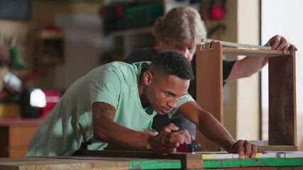 A Young Black Pupil Measuring Wood with Ruler at Workshop, Master Carpenter Taking Notes, Candid Scene of Carpenters Working