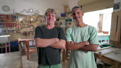 Brazilian Carpenters standing inside workshop smiling at camera, crossing arms. Portrait of Apprentice and Master Carpenter