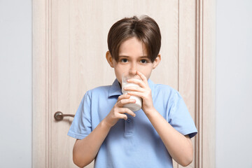 Little boy drinking fresh milk near door in room