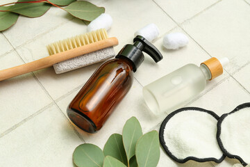 Bottles of cosmetic products, bath accessories and eucalyptus branches on light tile background
