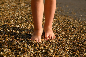 The legs of a boy or girl on the sand of the beach, covered with sand and beach pebbles. Children's...